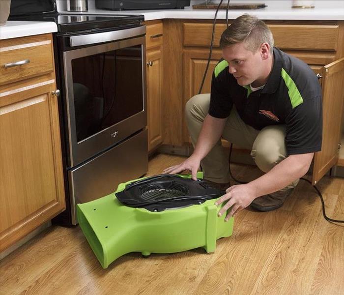 A man in SERVPRO gear placing an air mover in a kitchen 